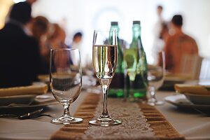 Champagne glass on a decorated table at a wedding or celebration with guests and drinks in the background