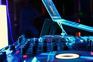 DJ mixing console with laptop and illuminated controls in a nightclub setting with blue and purple lighting.
