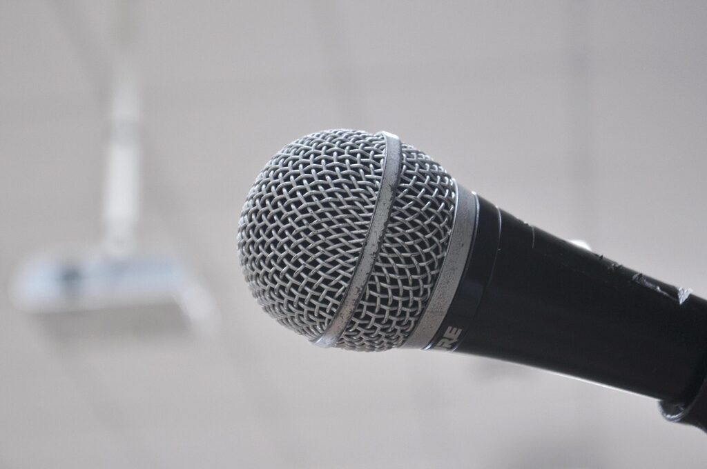 Close-up of a handheld microphone against a soft, blurred background, highlighting the metal mesh grille and black handle.
