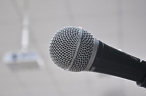 Close-up of a handheld microphone against a soft, blurred background, highlighting the metal mesh grille and black handle.