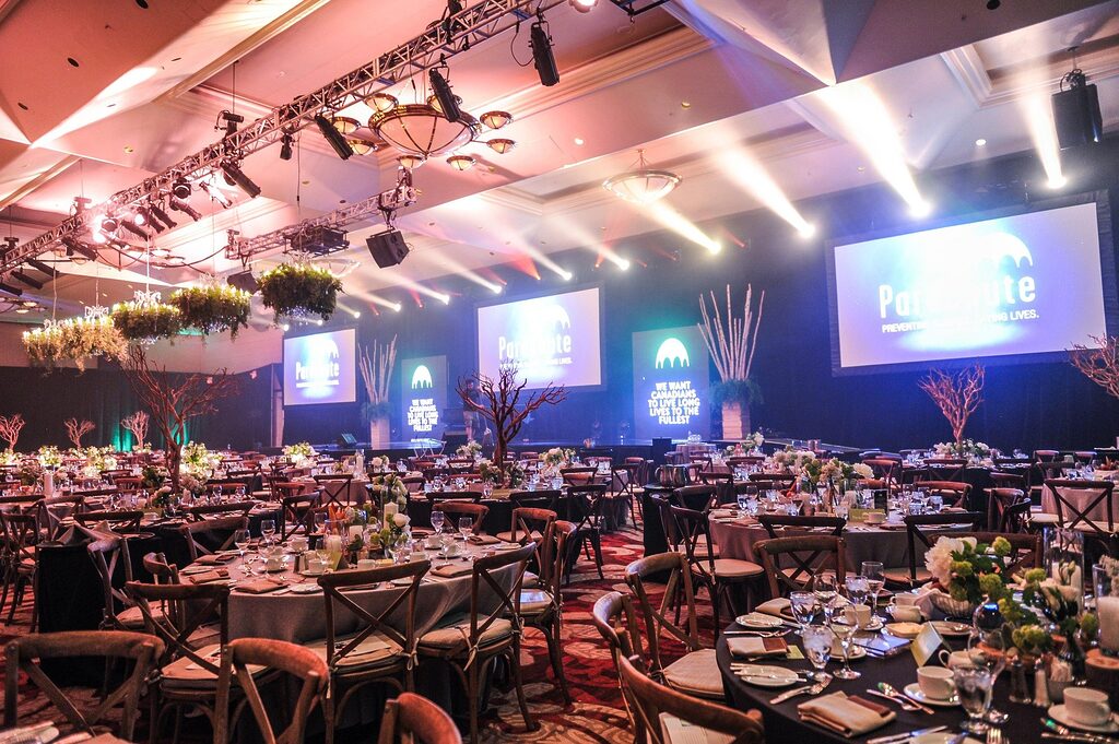 Large corporate event venue with banquet tables, stage lighting, LED screens and formal dining setup for conference or gala event