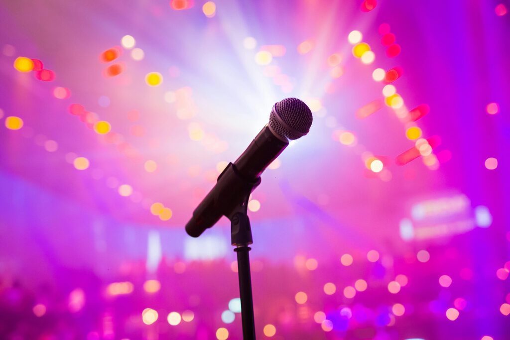 Microphone on stage with colourful lights and blurred crowd background during a live karaoke or music performance event