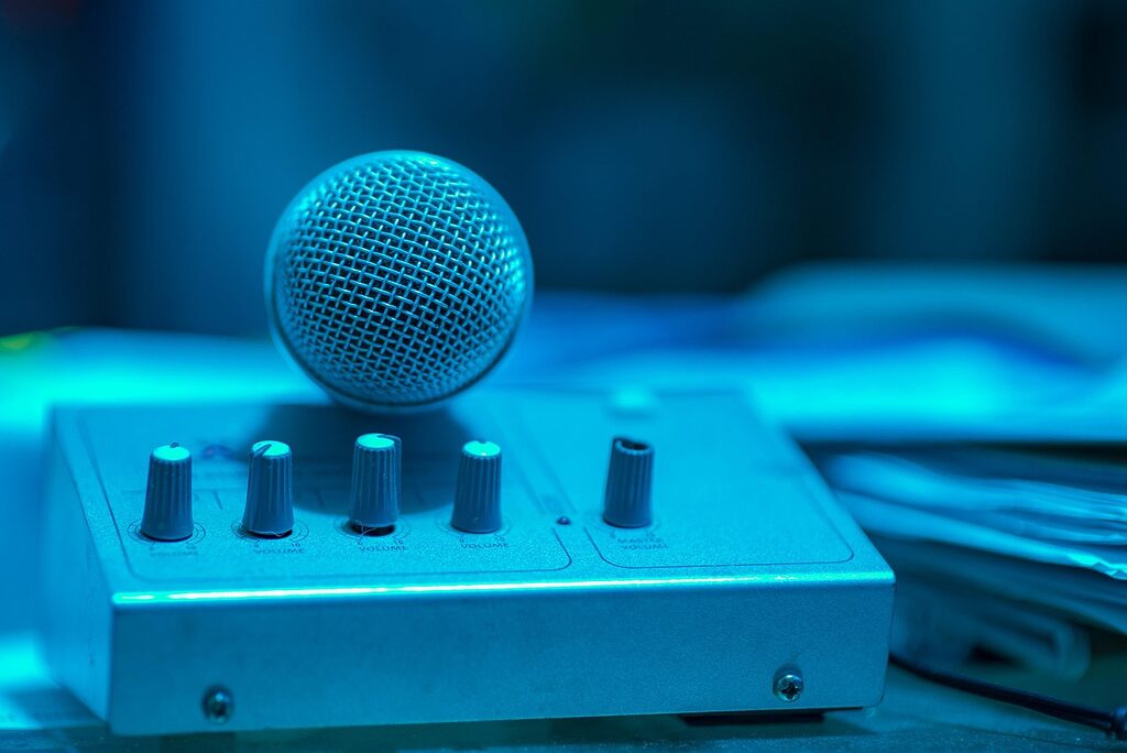 Close-up of a handheld microphone resting on an audio mixer with volume knobs, illuminated by cool blue lighting.