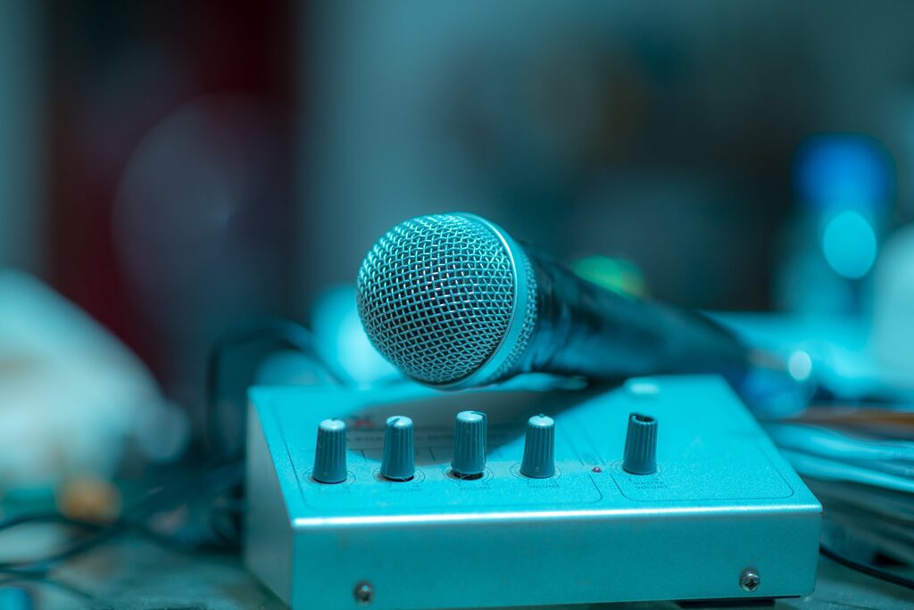 Close-up of a microphone resting on an audio mixer with control knobs, lit in blue tones with a blurred background.