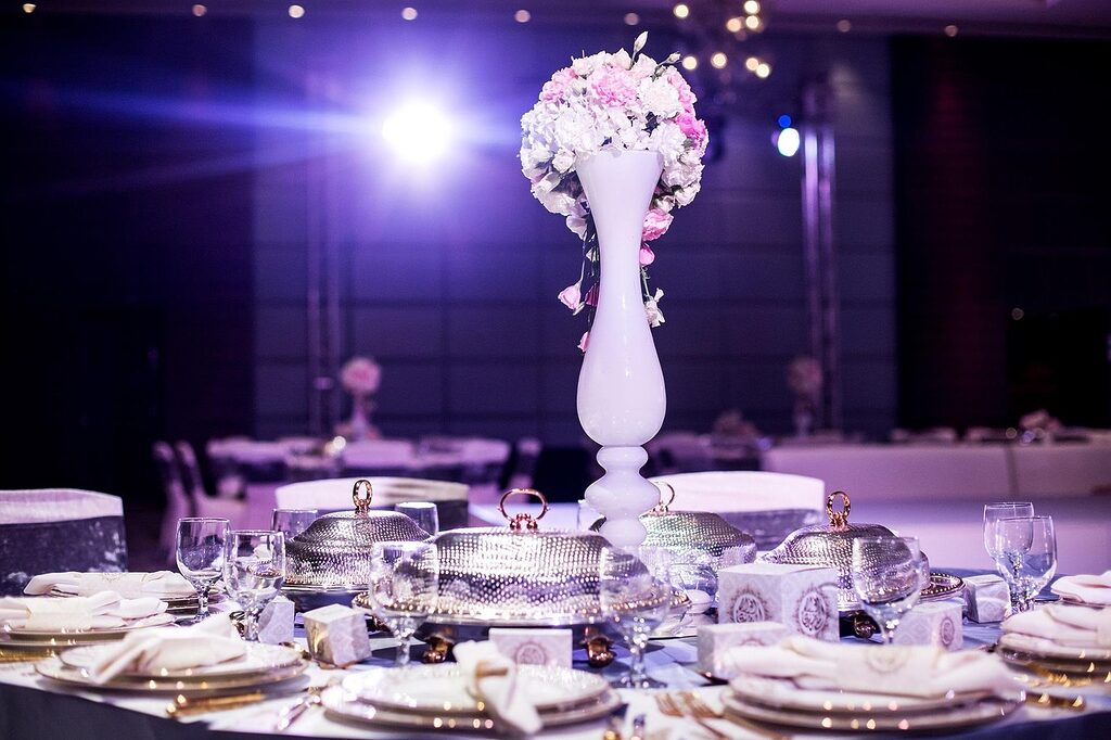 Elegant wedding reception table with tall floral centrepiece, place settings and ambient event lighting in a decorated venue