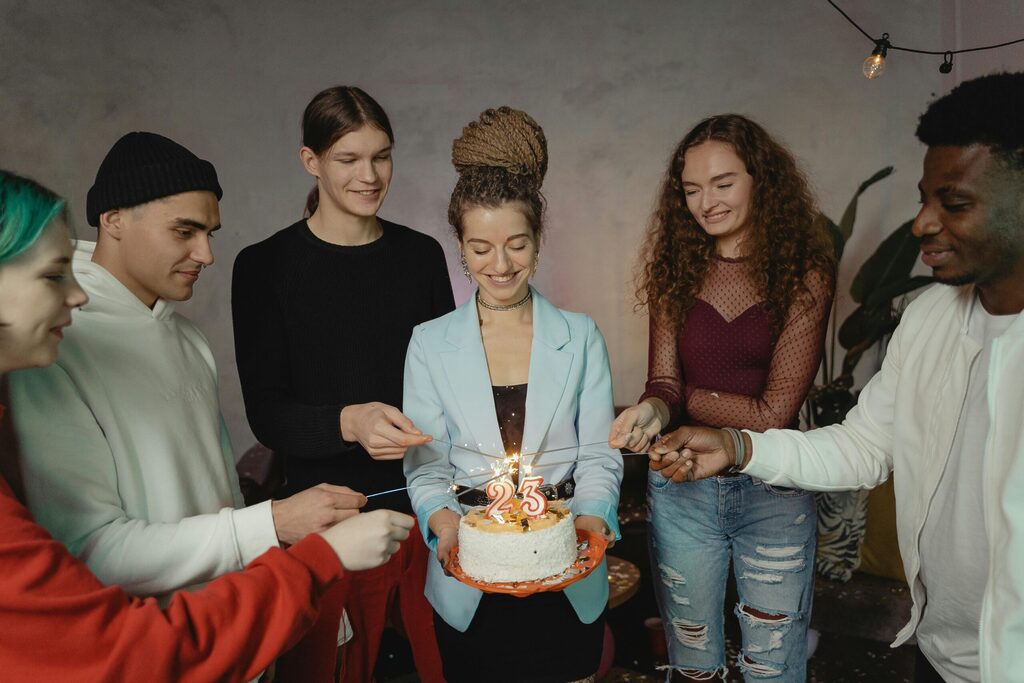 birthday party with group of friends celebrating their birthday friend with birthday cake and number 23 candles